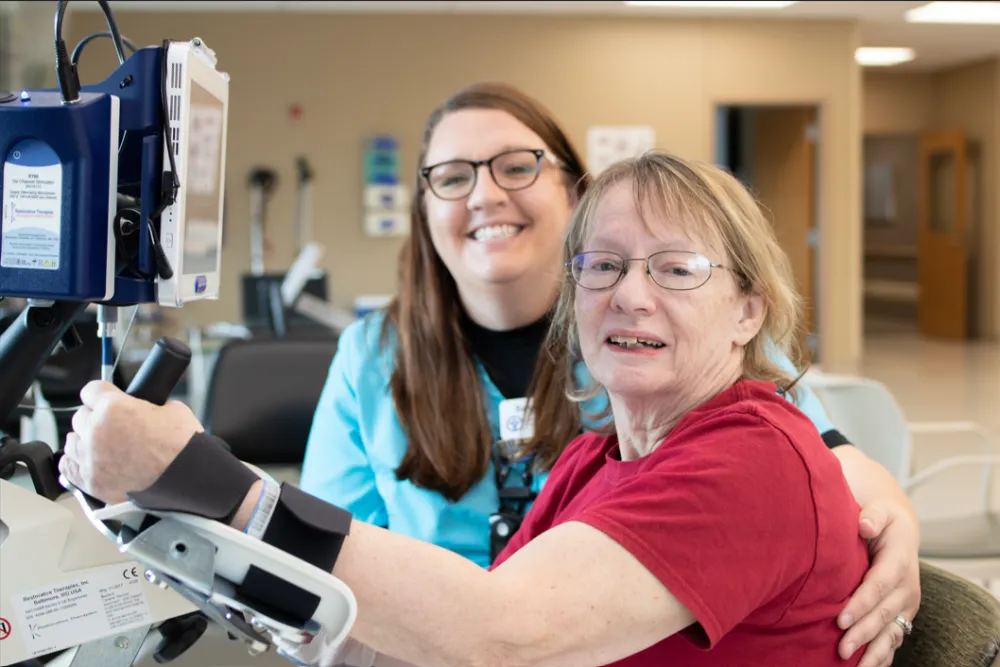 Woman in red shirt using rehabilitation equipment with the support of a Reid Health therapist.