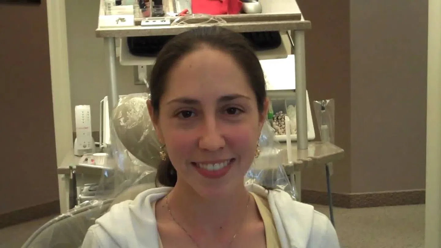 Smiling woman with dark hair sitting in a dental office chair in a dental clinic environment.