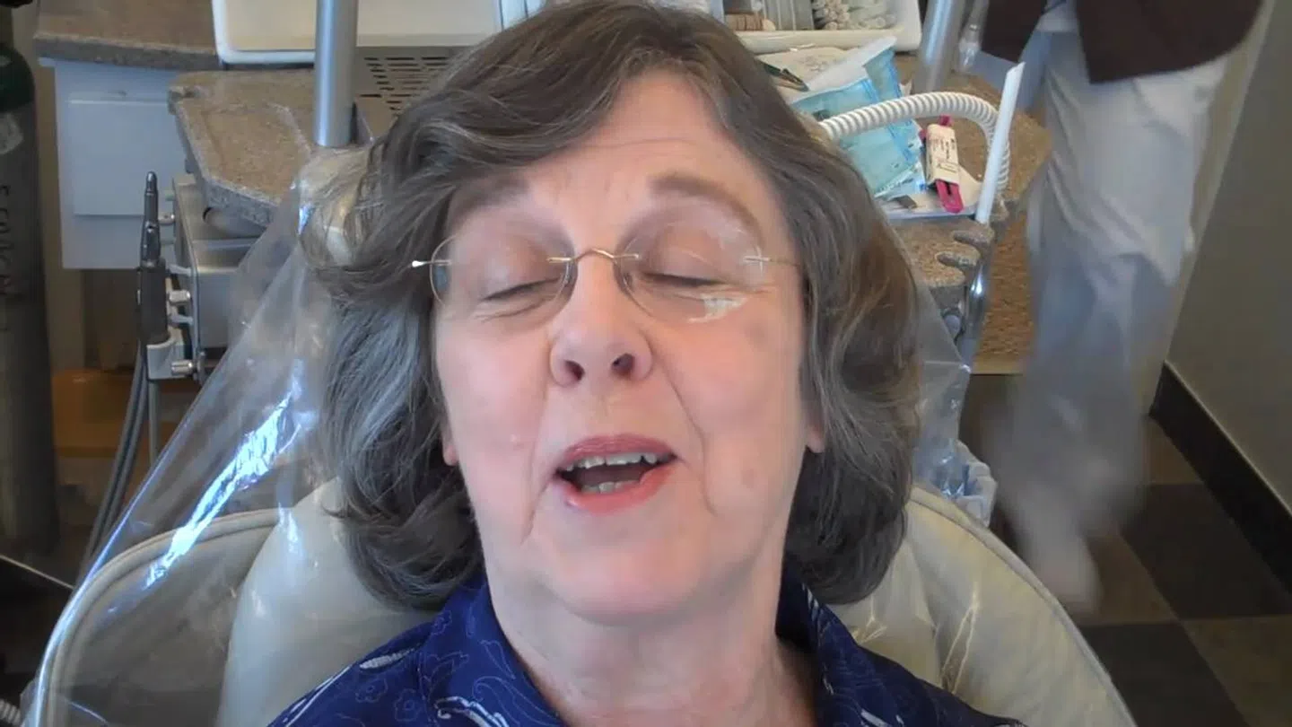 Elderly woman with glasses sitting in a dental chair with eyes closed and mouth slightly open.