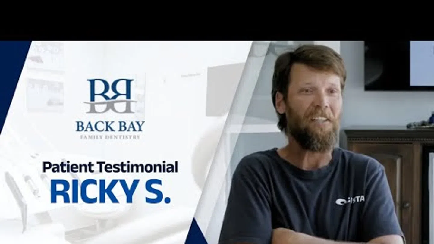 Smiling man with beard shares a patient testimonial for Back Bay Family Dentistry in a bright office setting