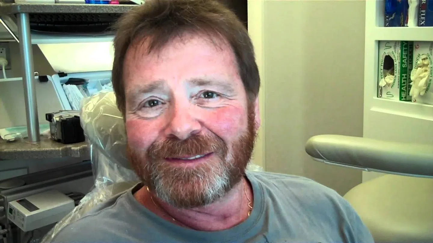 Smiling middle-aged man with beard sitting in a dental office chair with dental equipment in the background