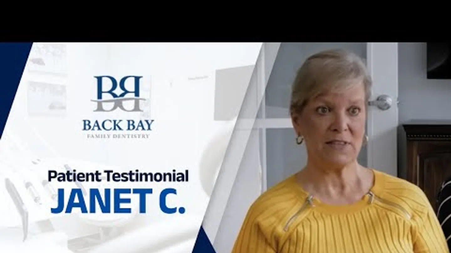 Patient Janet C. giving testimonial for Back Bay Family Dentistry, wearing a yellow top in a home setting.