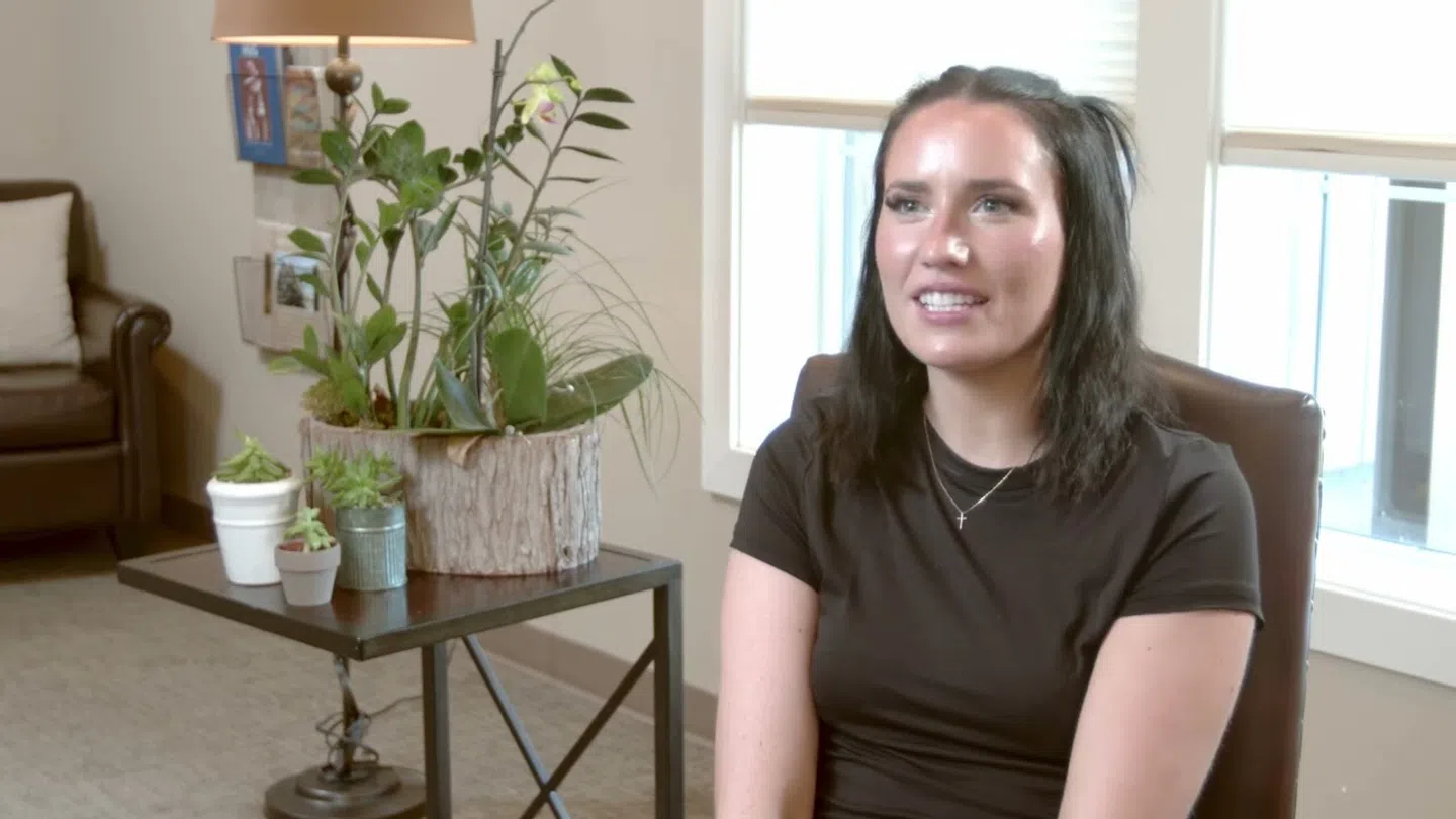 Young woman with dark hair sitting in an office chair near a window and a table with houseplants.