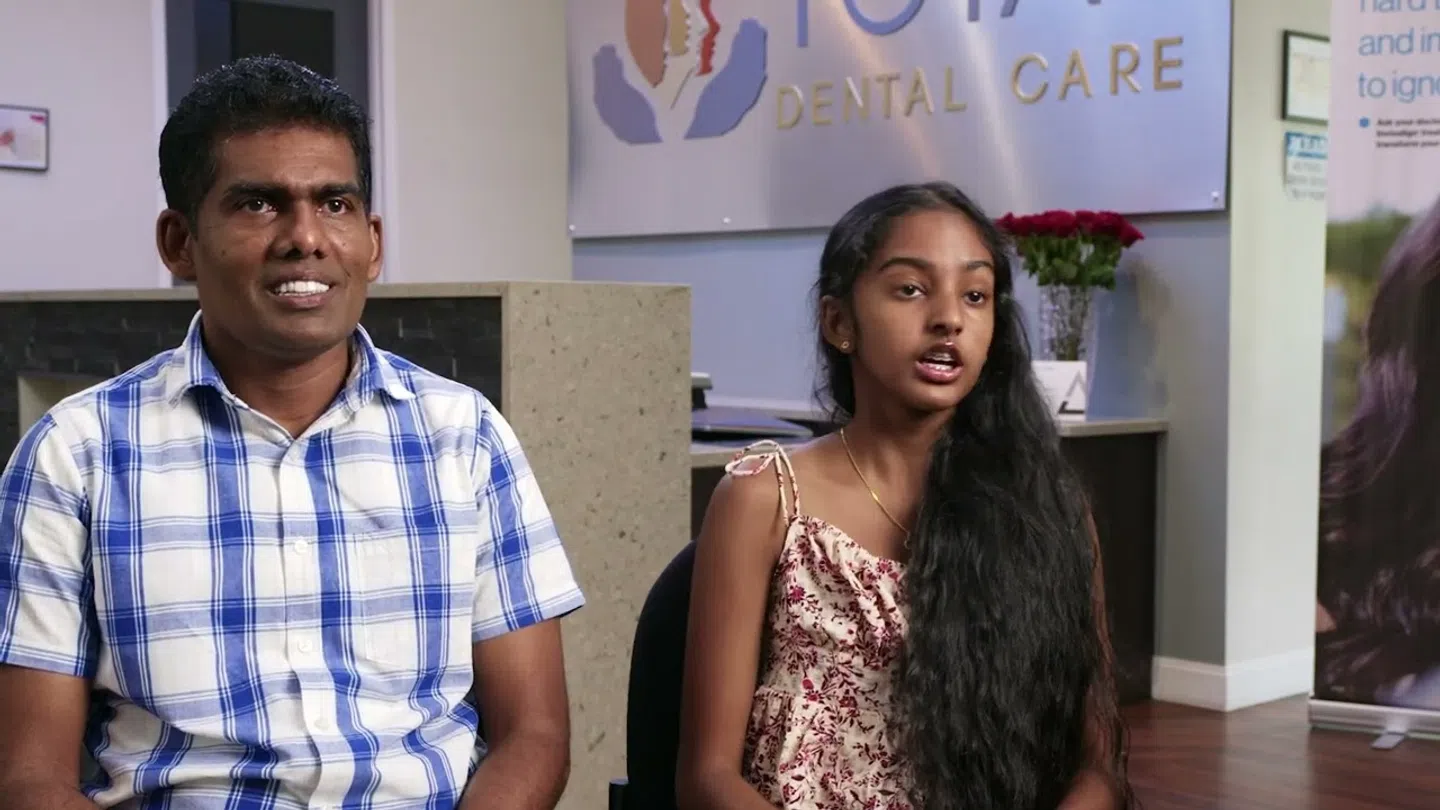 Man and girl sitting in a dental clinic reception area with a dental care sign in the background