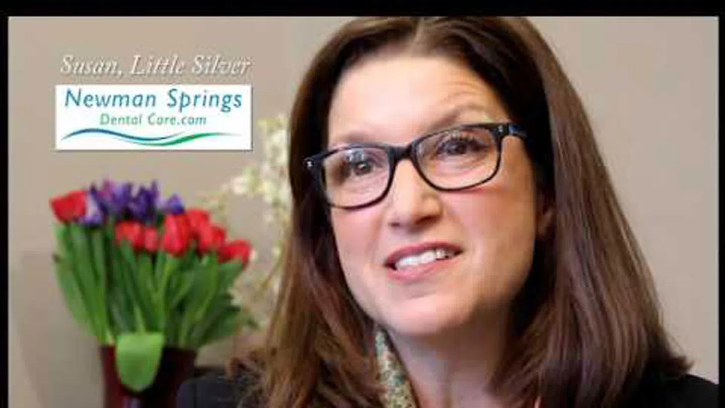 Woman with glasses smiling, Newman Springs Dental Care logo and red and purple flowers in background
