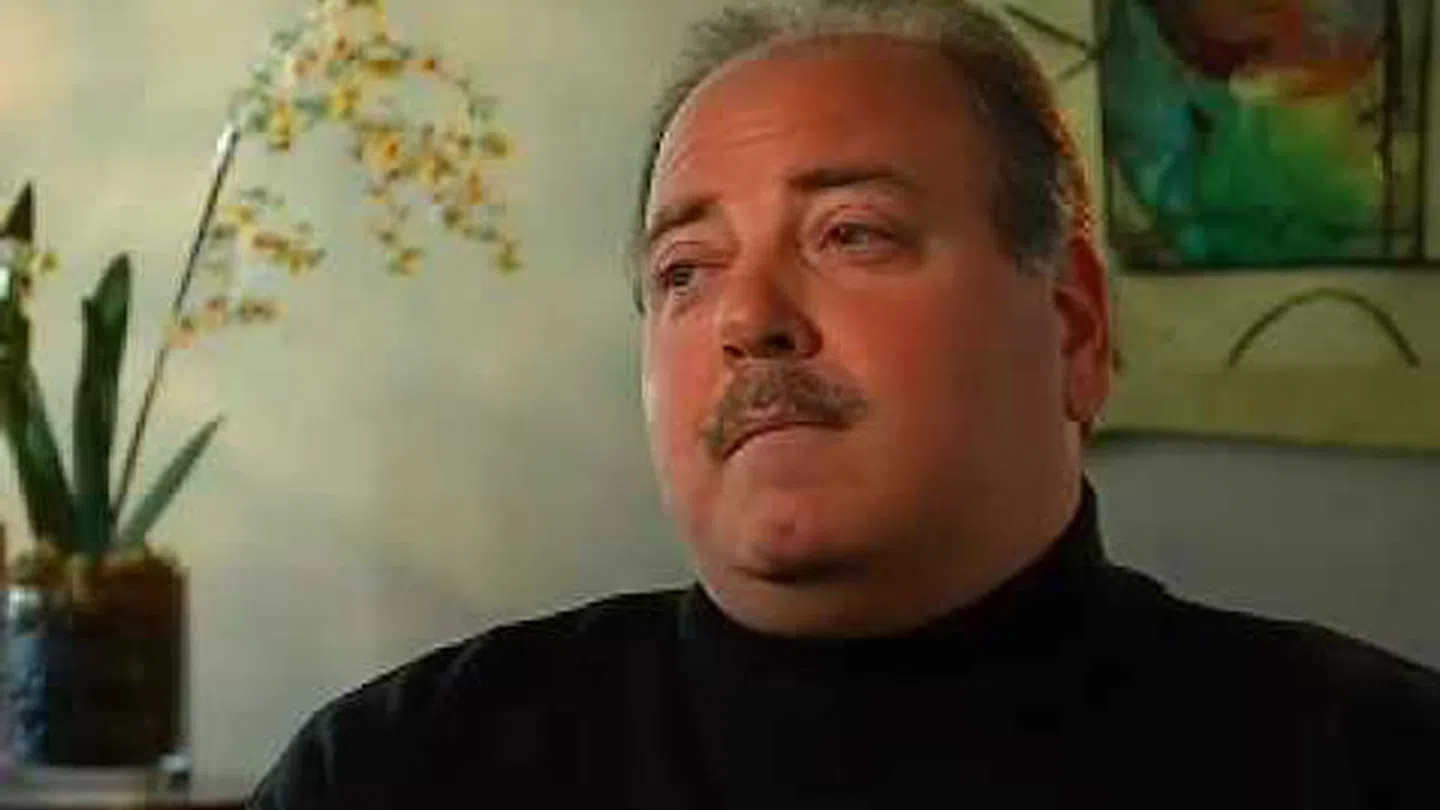 Portrait of a middle-aged man with mustache wearing a black turtleneck, looking to the side indoors