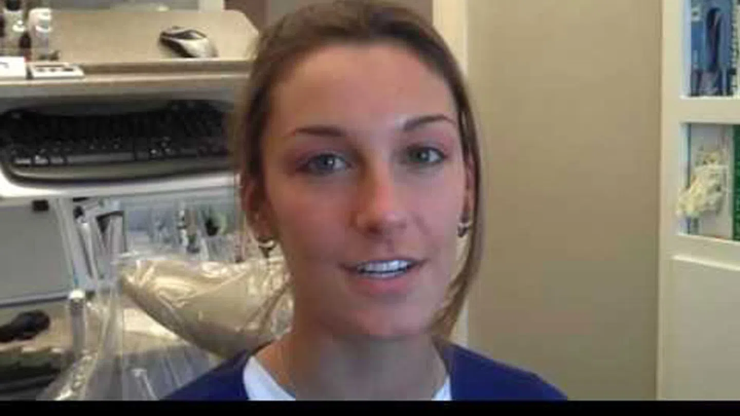 Young woman smiling in a dental office with dental chair and equipment in background.