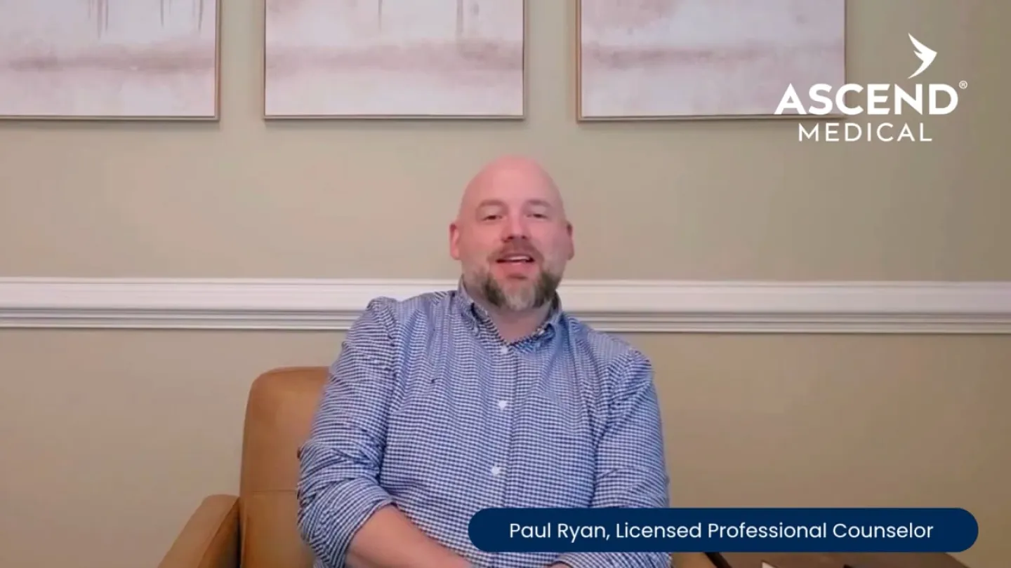 Licensed counselor Paul Ryan sitting on a brown leather chair in a room with light wall art and Ascend Medical logo.