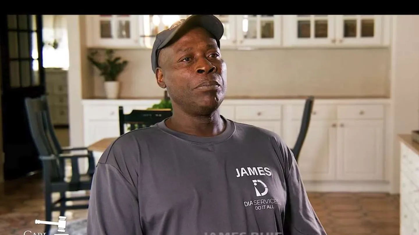 Man wearing a James Dia Services Do It All shirt sitting in a kitchen with white cabinets and chairs.