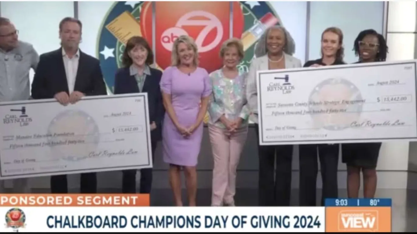 Group of people holding large donation checks on Chalkboard Champions Day of Giving 2024 broadcast