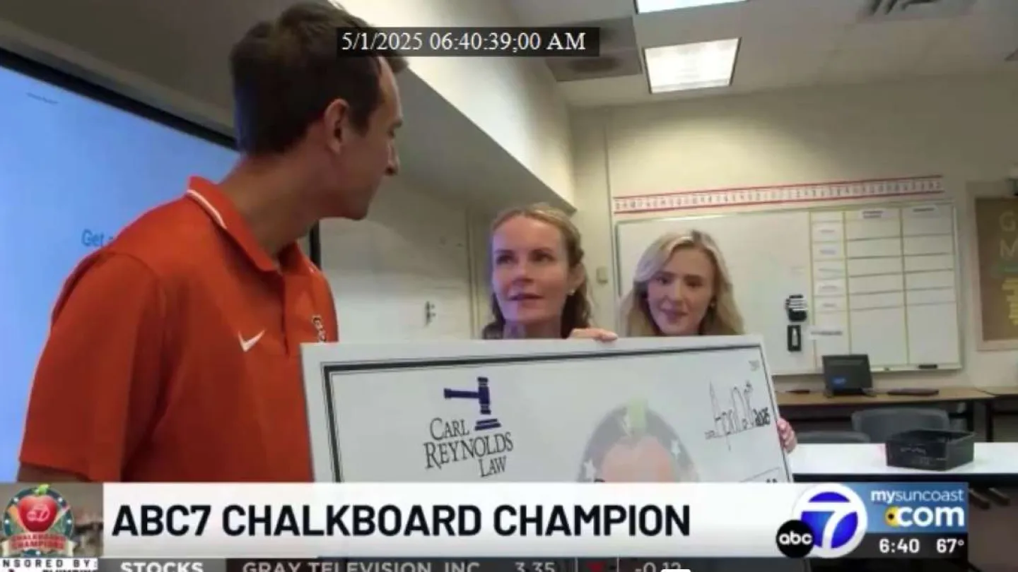 Three people in a classroom holding a large check for ABC7 Chalkboard Champion award presentation.