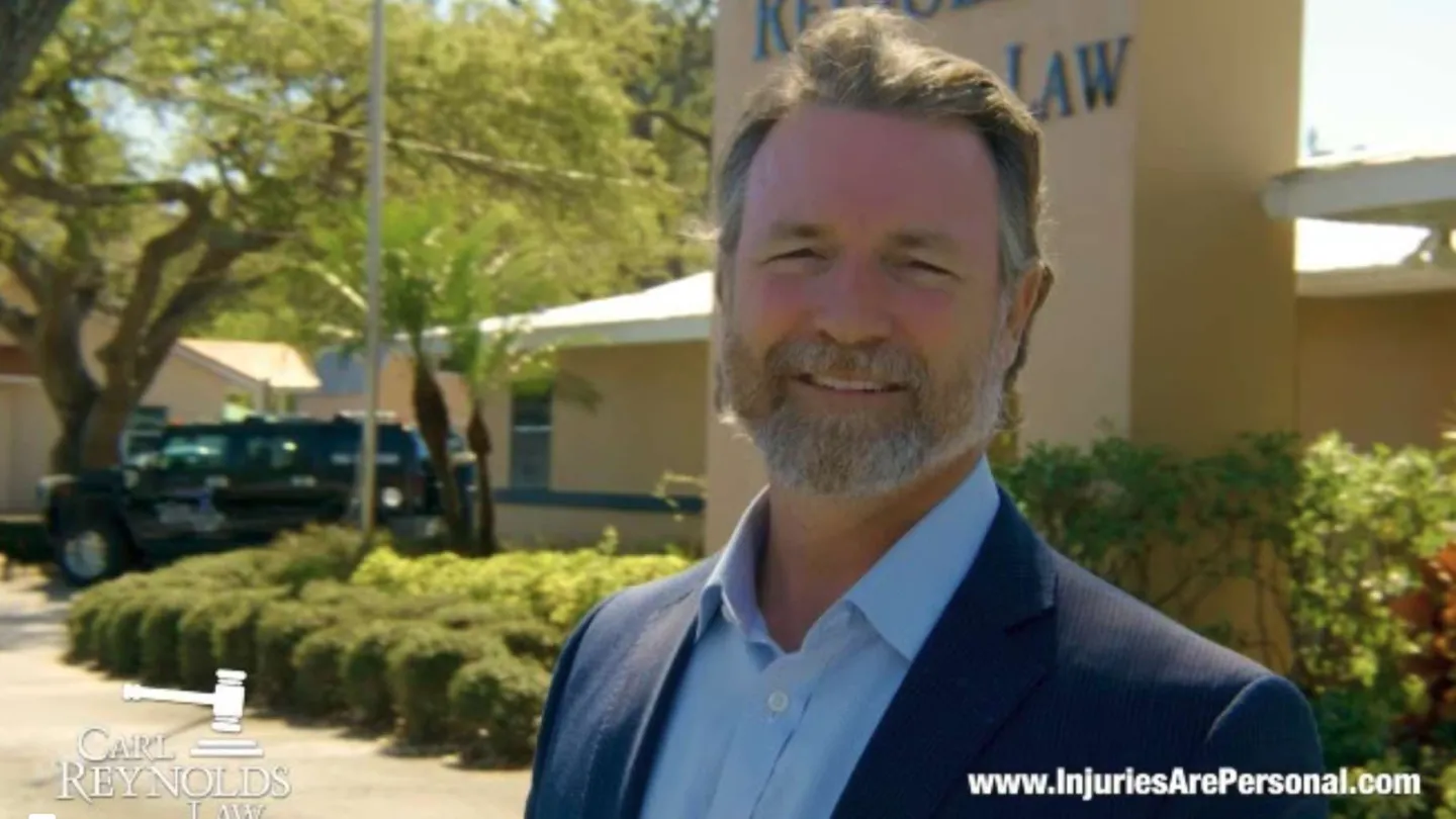 Smiling man in suit standing outside the law office of Campi Reynolds during a sunny day