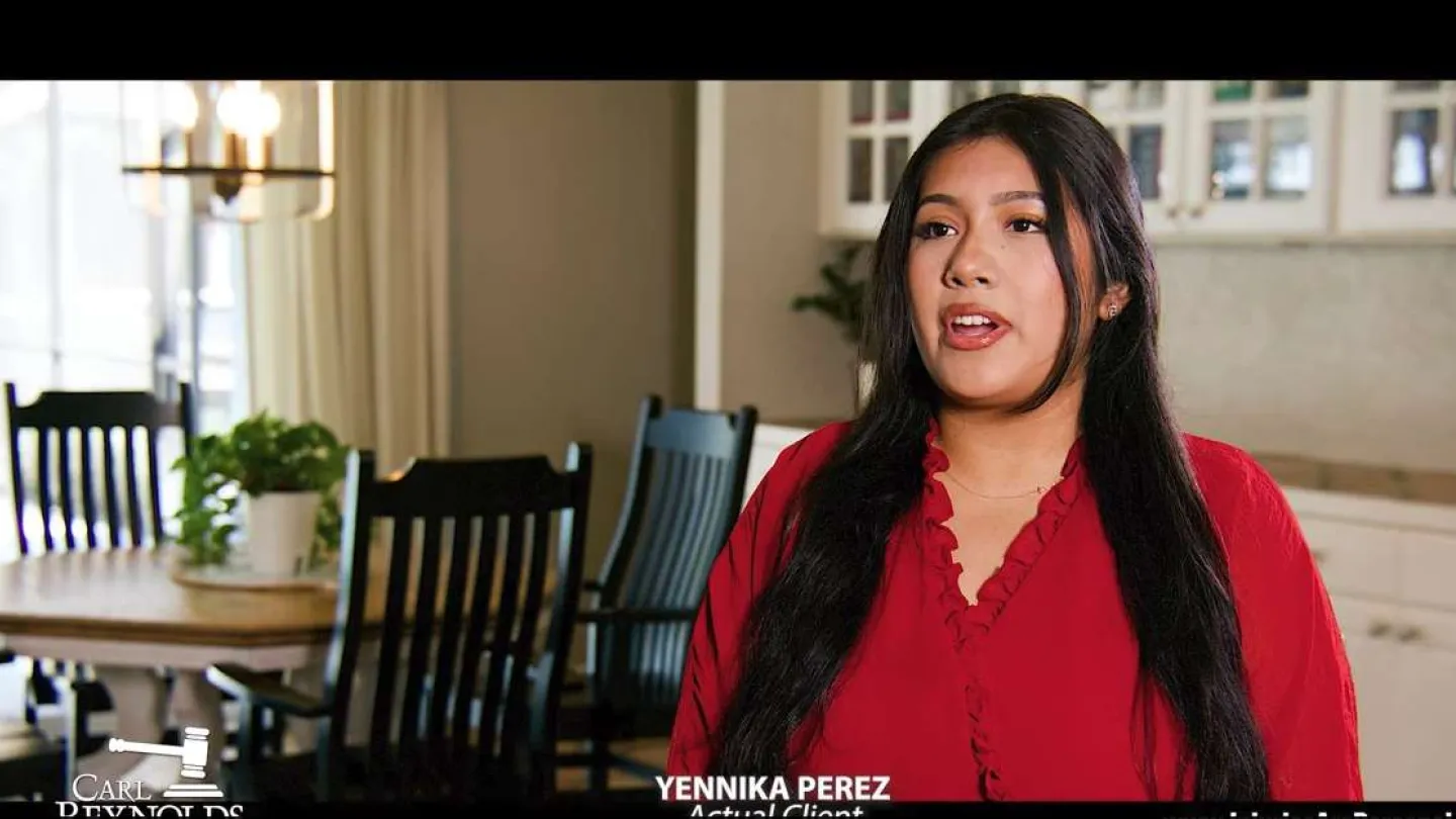 Woman with long dark hair wearing a red blouse speaking inside a bright dining room with black chairs and a wooden table.