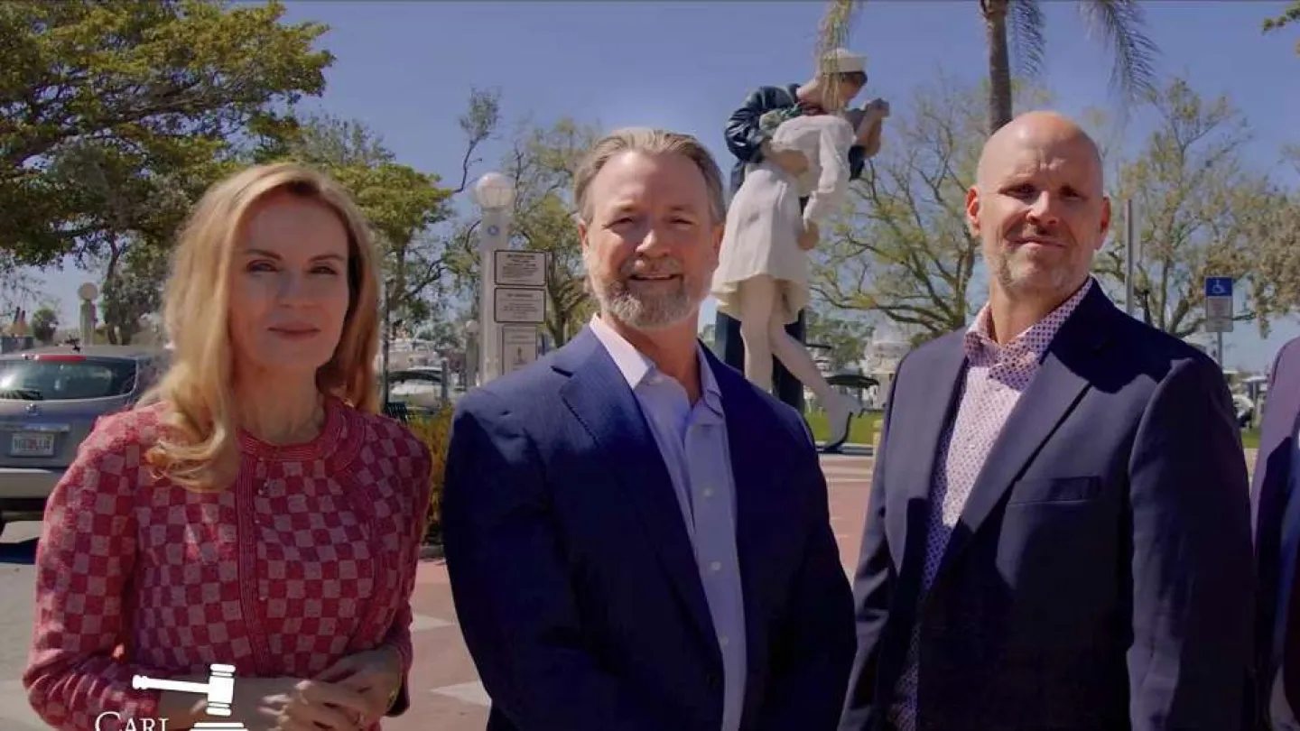 Four professionals in business attire standing outdoors with trees and blue sky in the background
