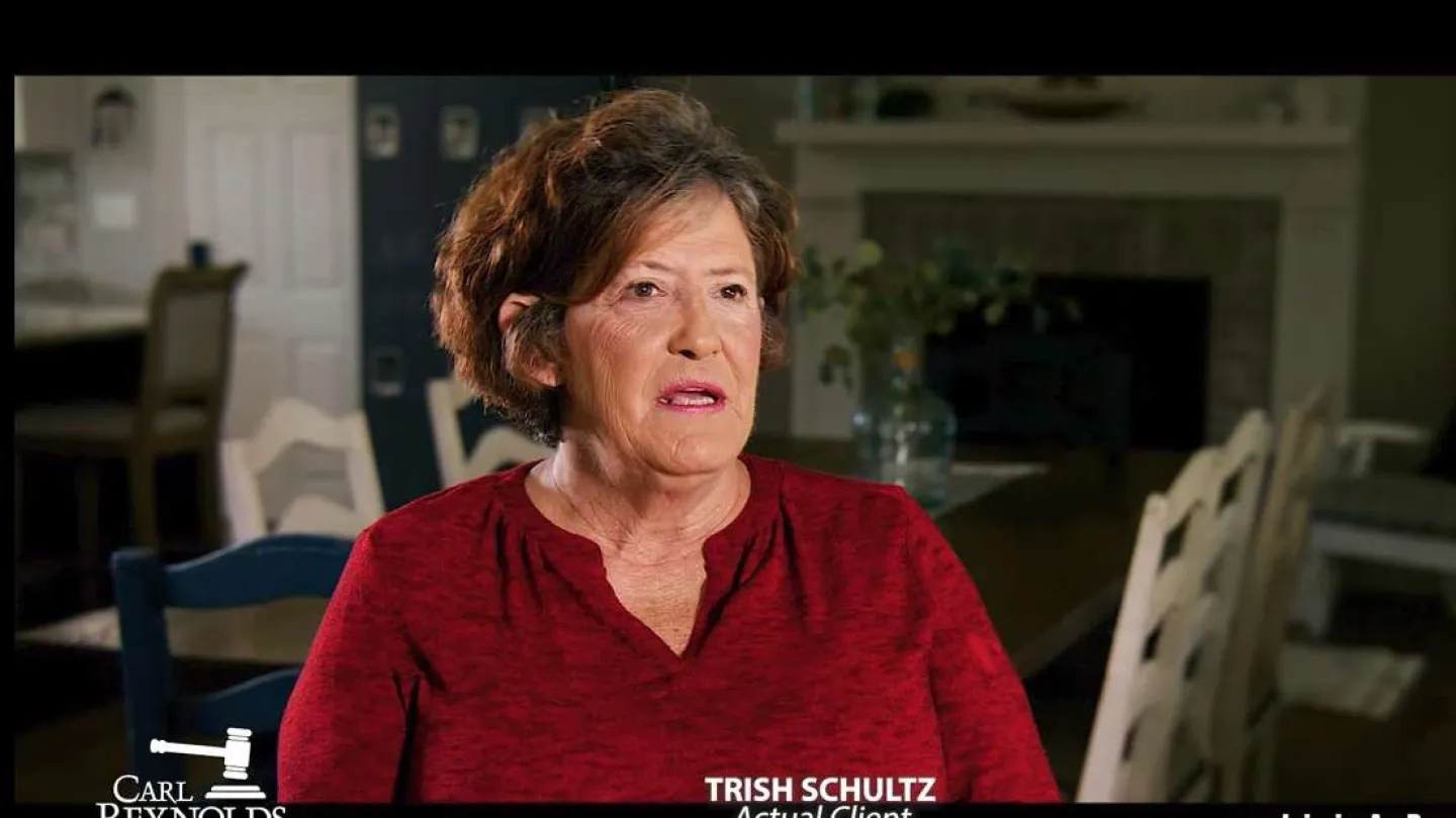 Middle-aged woman in red shirt speaking in a warmly lit dining room with white chairs and dark walls.