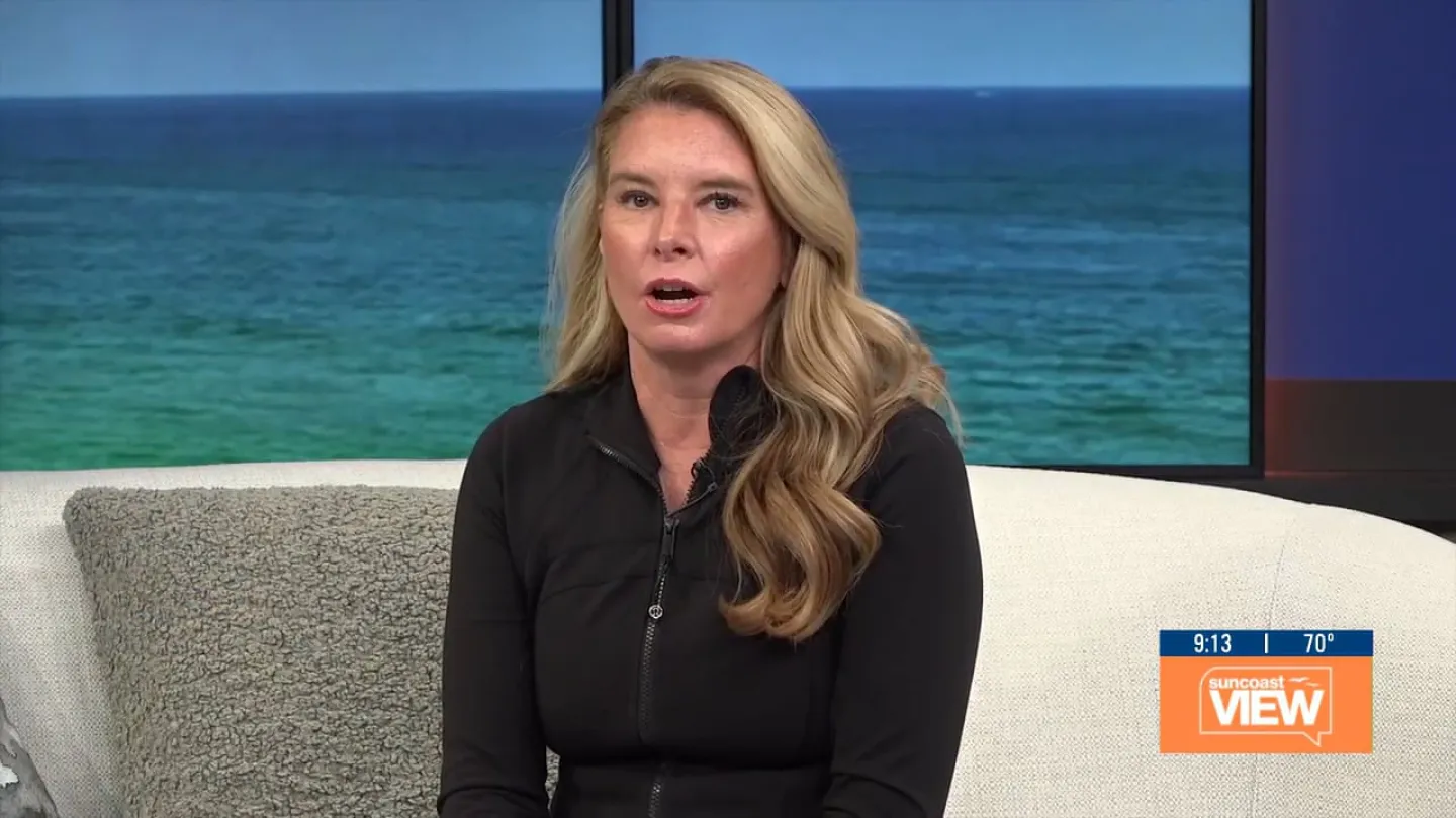 Woman with long blonde hair speaking on Suncoast View show with ocean backdrop and cozy couch.