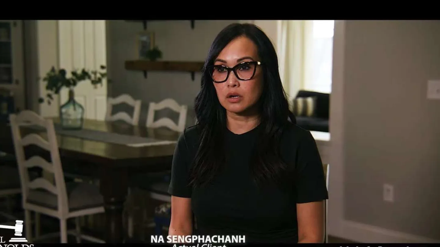 Woman with glasses speaking in a modern dining room with white chairs and wooden table in background