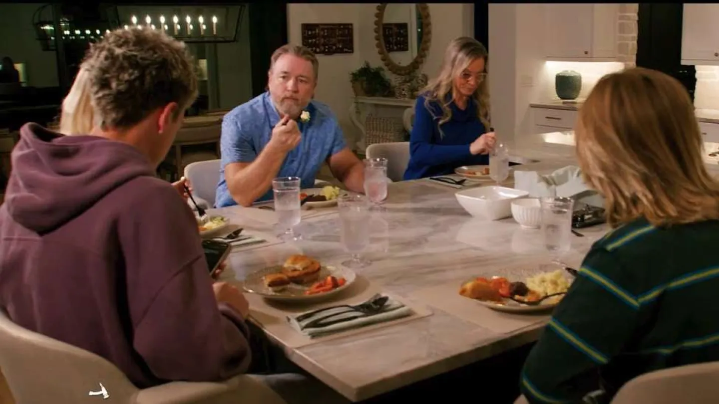 Family and friends sharing a meal at a modern kitchen dining table with plates of food and drinks.