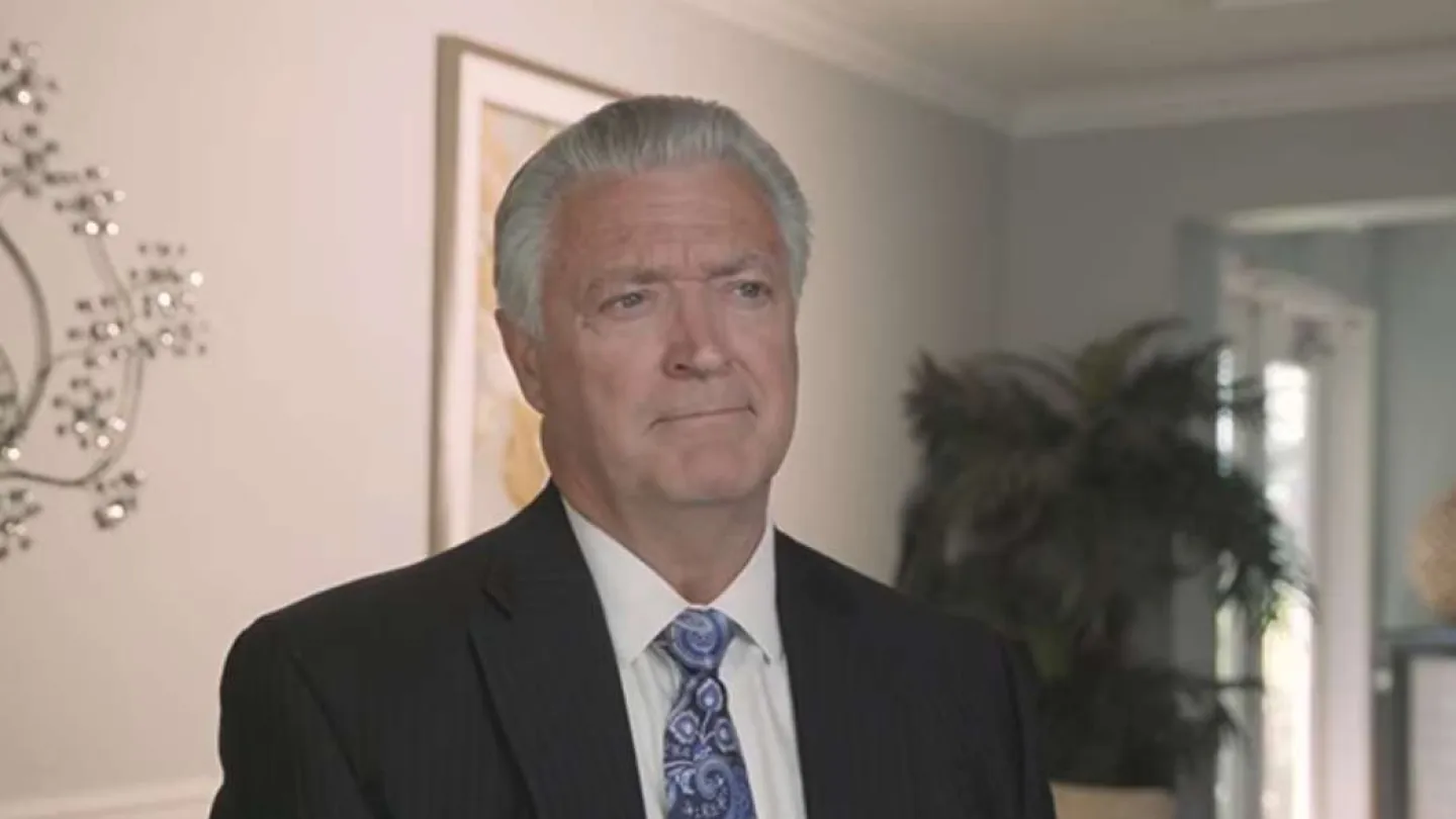 Mature businessman with gray hair wearing a suit and paisley tie in a professional office setting.