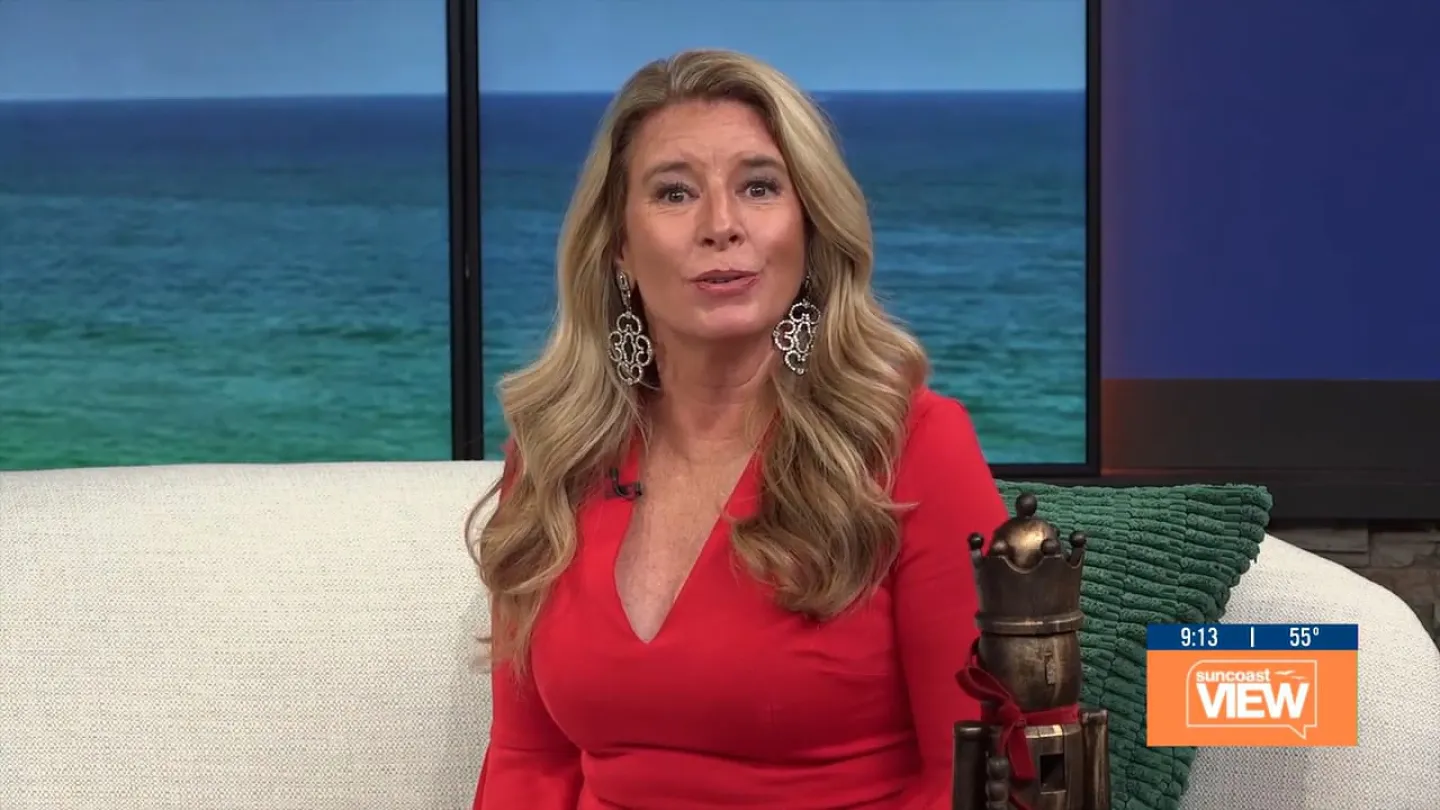 Woman in red dress speaking on a couch with ocean backdrop and Suncoast View logo on screen