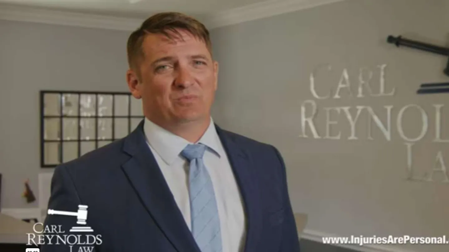 Professional male lawyer in suit standing in office with Carl Reynolds Law logo and website in background