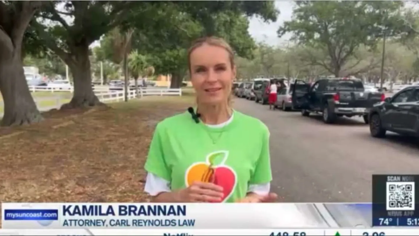 Attorney Kamila Brannan speaking outdoors near parked cars and trees during a news segment