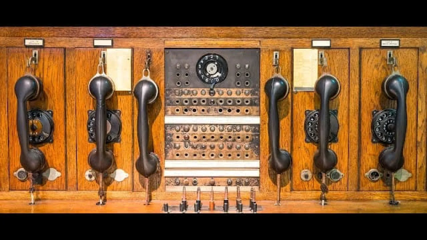 Vintage wooden telephone switchboard with multiple black handsets and rotary dial in the center.