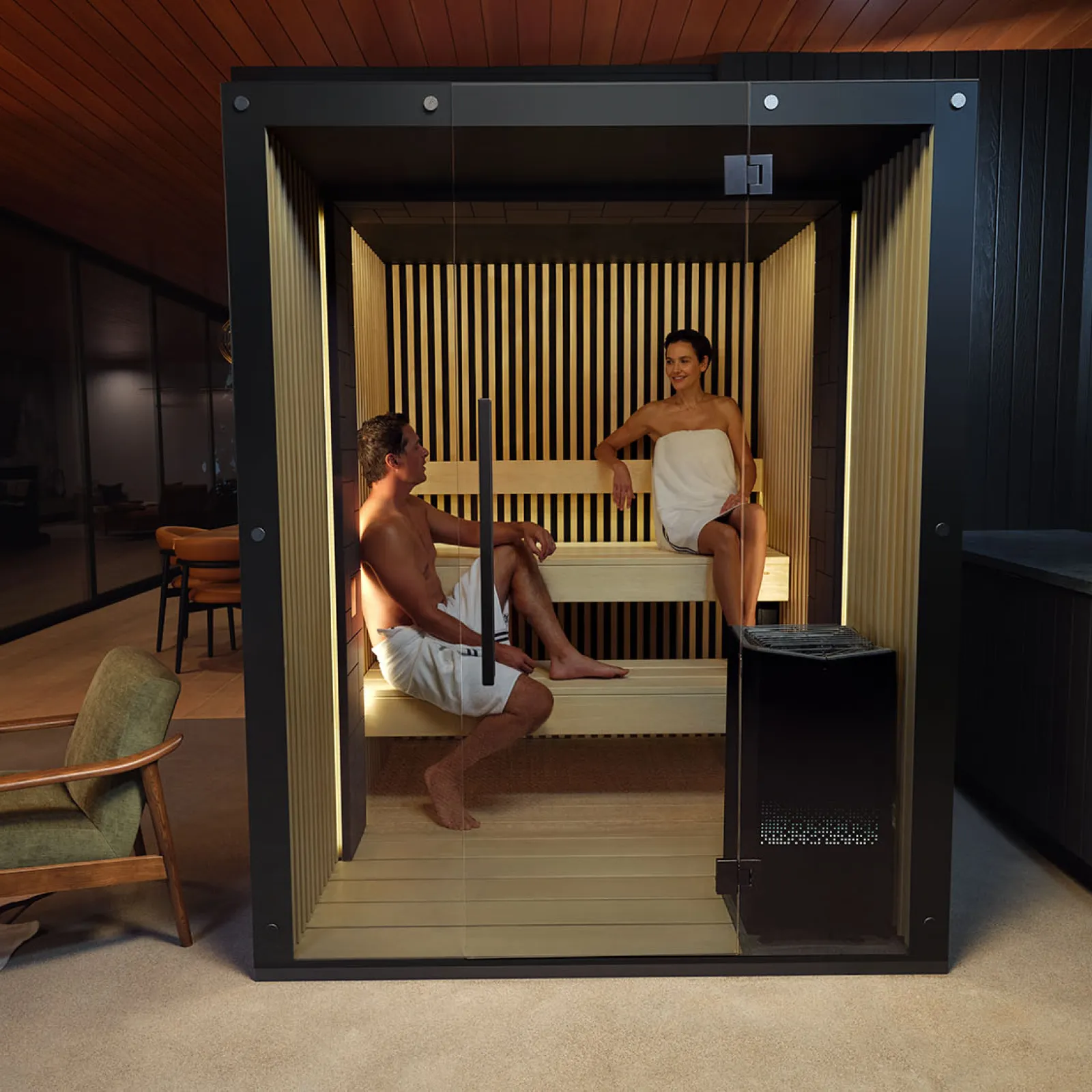 a man and woman sitting on a bench in a room with a wood floor and a black box