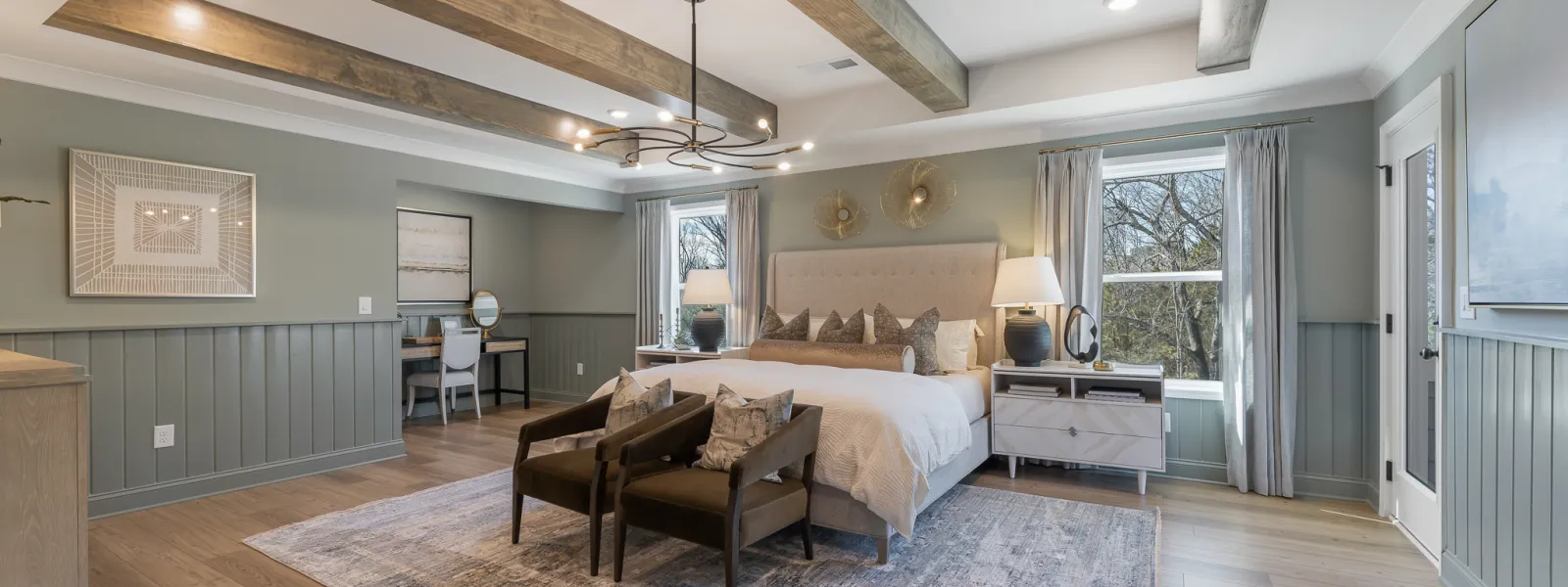 Spacious bedroom with wood beams, large rug, seating area, neutral tones, and natural light through windows.