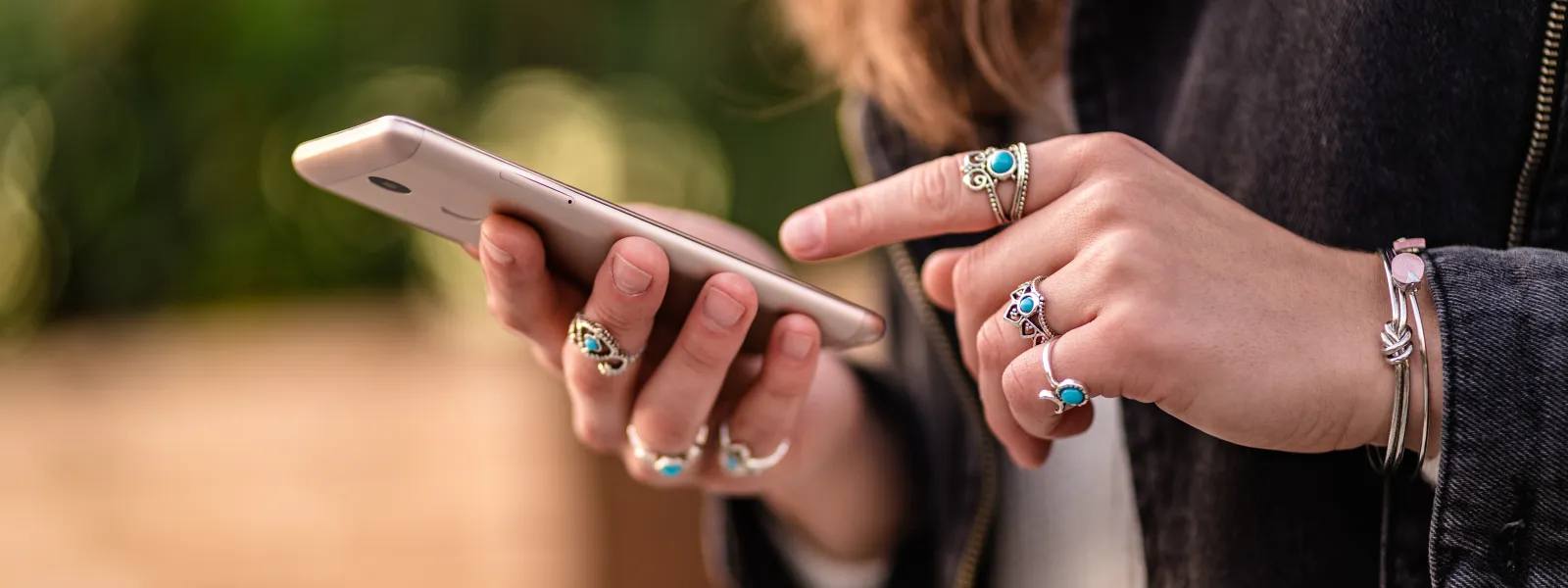 a woman with lots of rings on her hands holding a smartphone