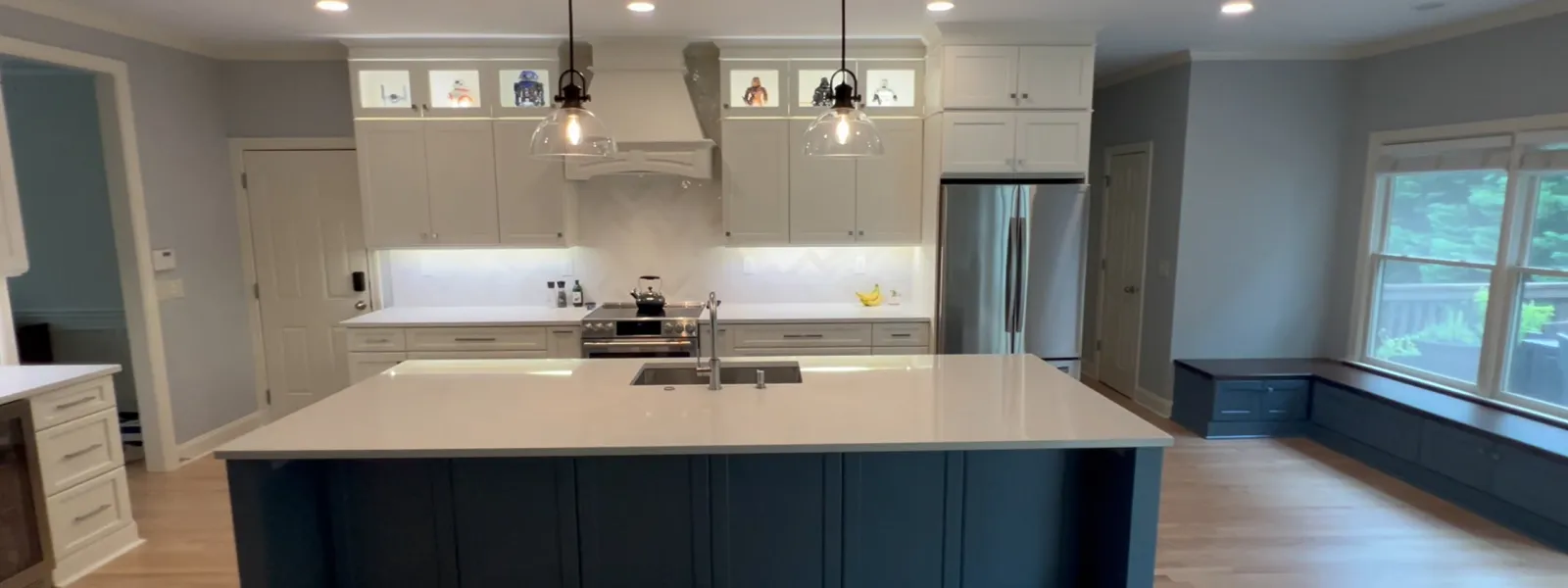 Modern kitchen with large white island, navy base, pendant lights, stainless appliances, and window seating.