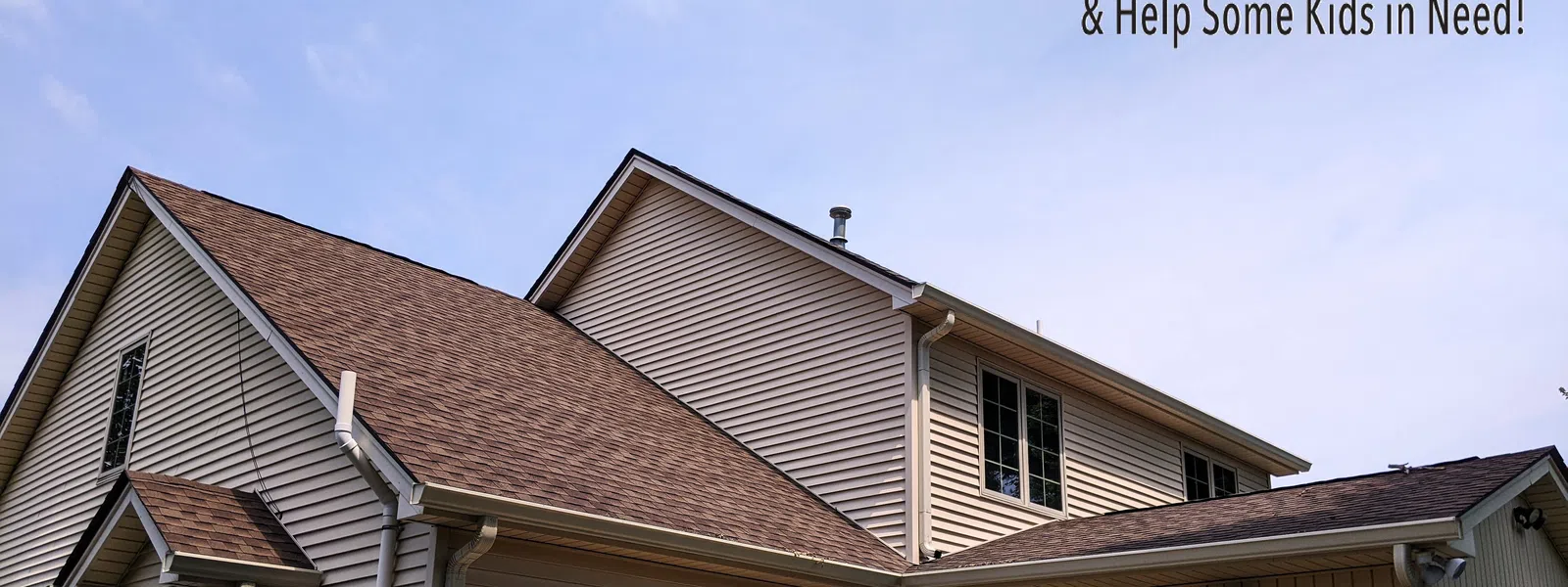 New tan shingle roof on beige two-story house under clear blue sky with charity Roof It Forward logo in corner.