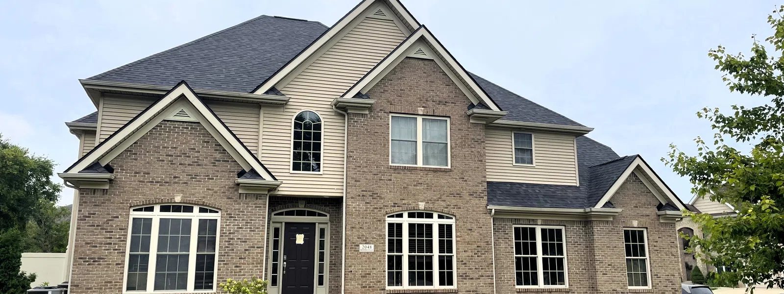 Large two-story brick and siding house with a dark shingled roof and a well-maintained green lawn..
