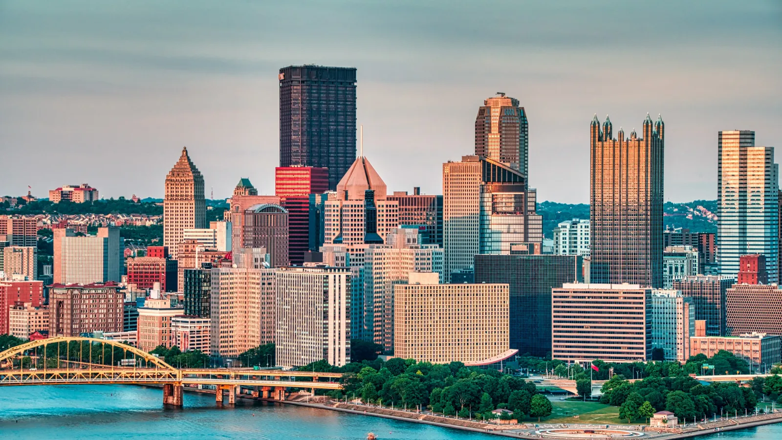 Pittsburgh skyline with rivers, green spaces, and bridges under a clear sky at sunset