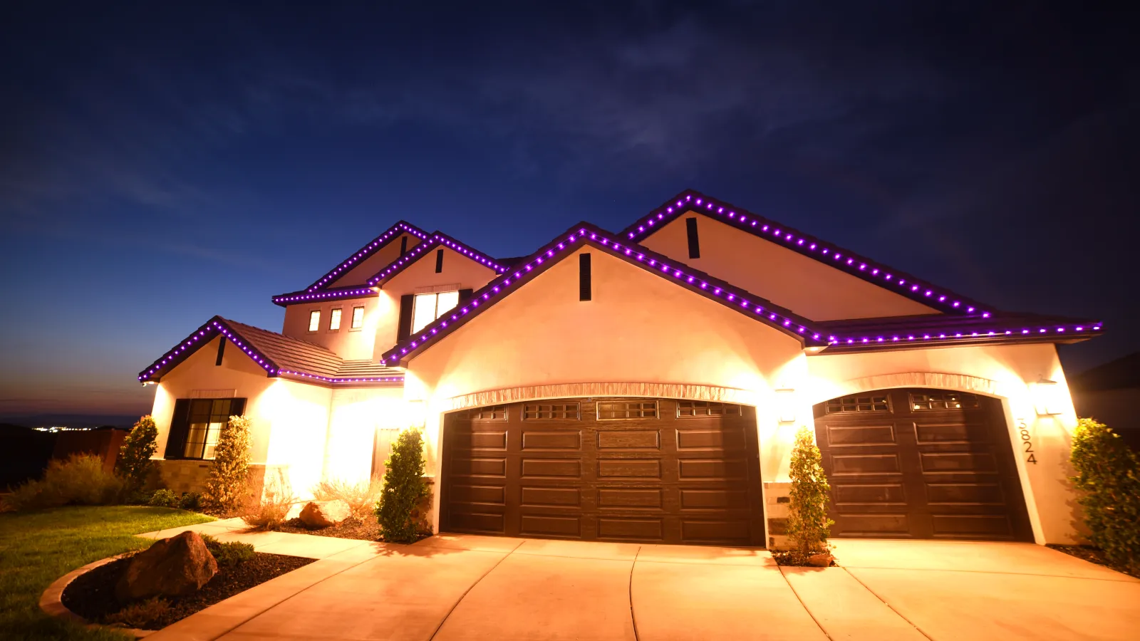 Modern house at dusk with purple LED lights outlining roof edges and illuminated garage doors.