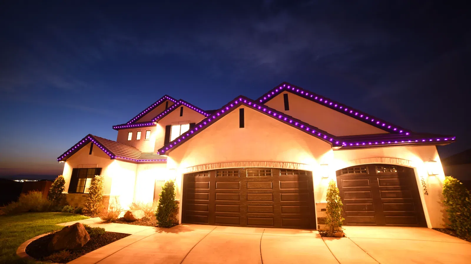 Modern suburban house at dusk with purple LED lights outlining the roof and a three-car garage visible.