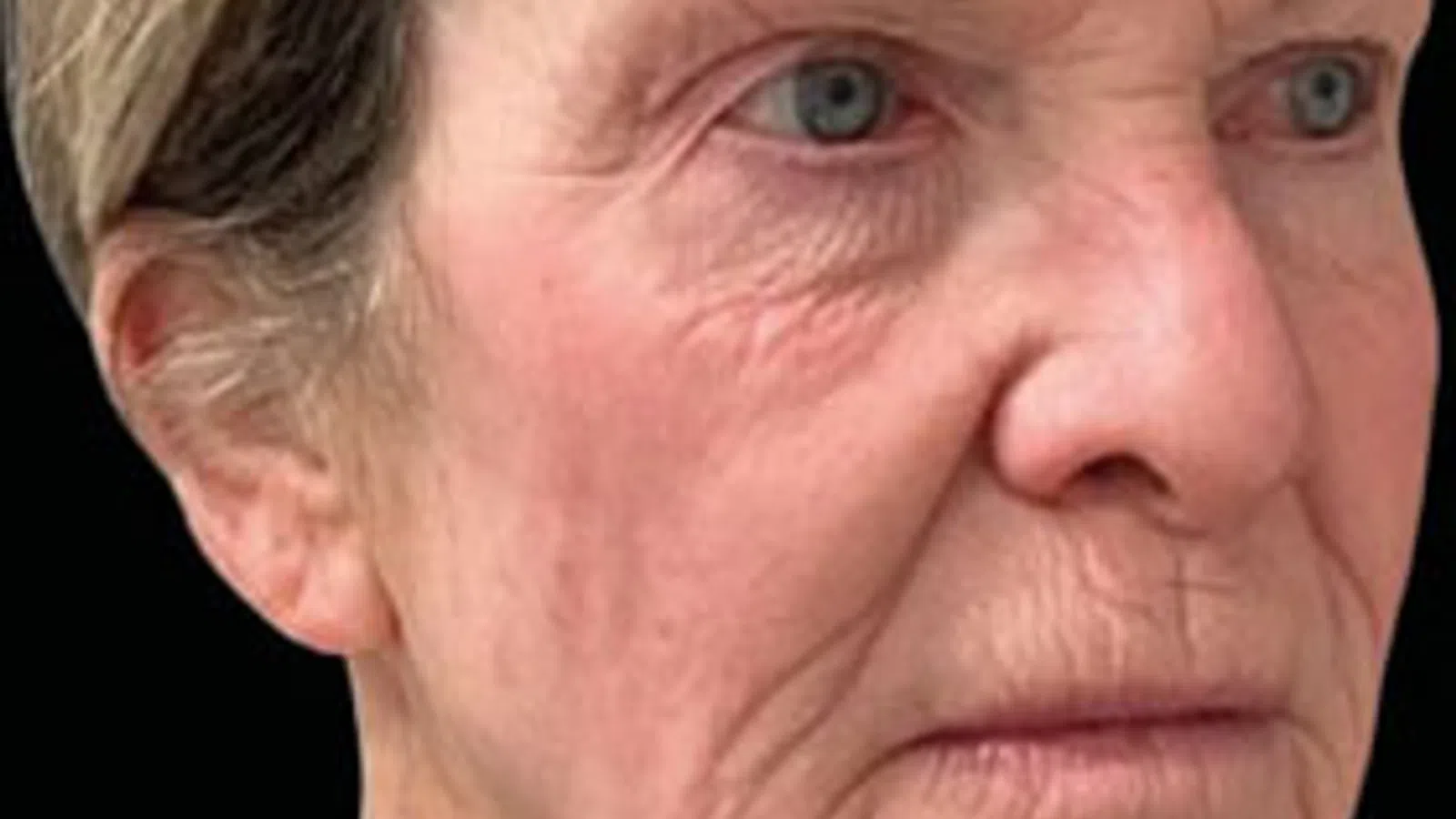 Close-up of elderly woman's face showing wrinkles, light blue eyes, and short gray hair with hairpin.