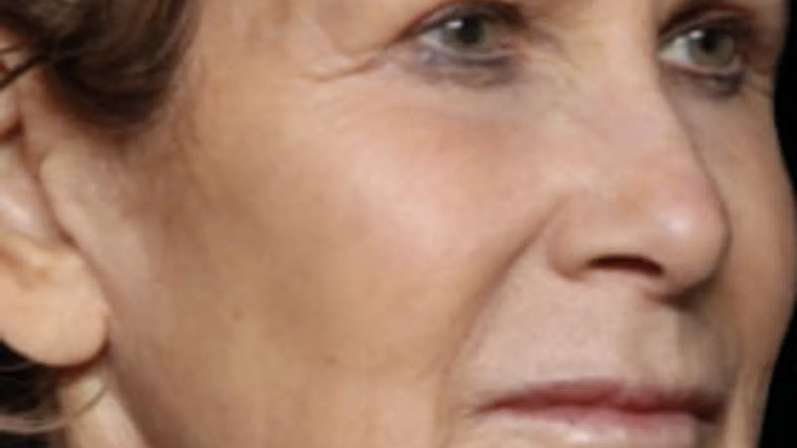 Close-up profile of an older woman’s face showing natural skin texture and expression against a black background