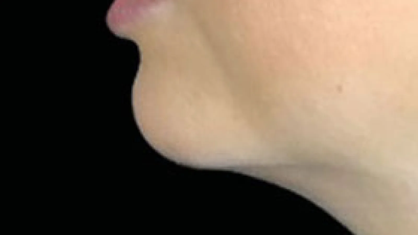 Close-up side profile of a person's lower face, nose, lips, and chin against a black background