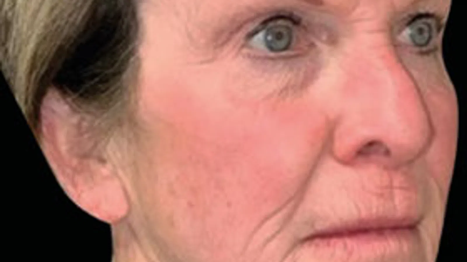 Close-up of an elderly woman with gray hair, light blue eyes, and visible wrinkles on her face and neck.