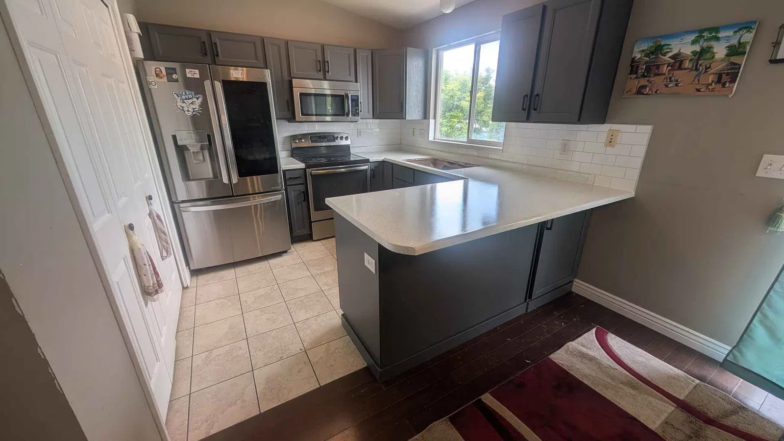 Modern kitchen with gray cabinets, stainless steel appliances, white countertops, tile and dark wood flooring.