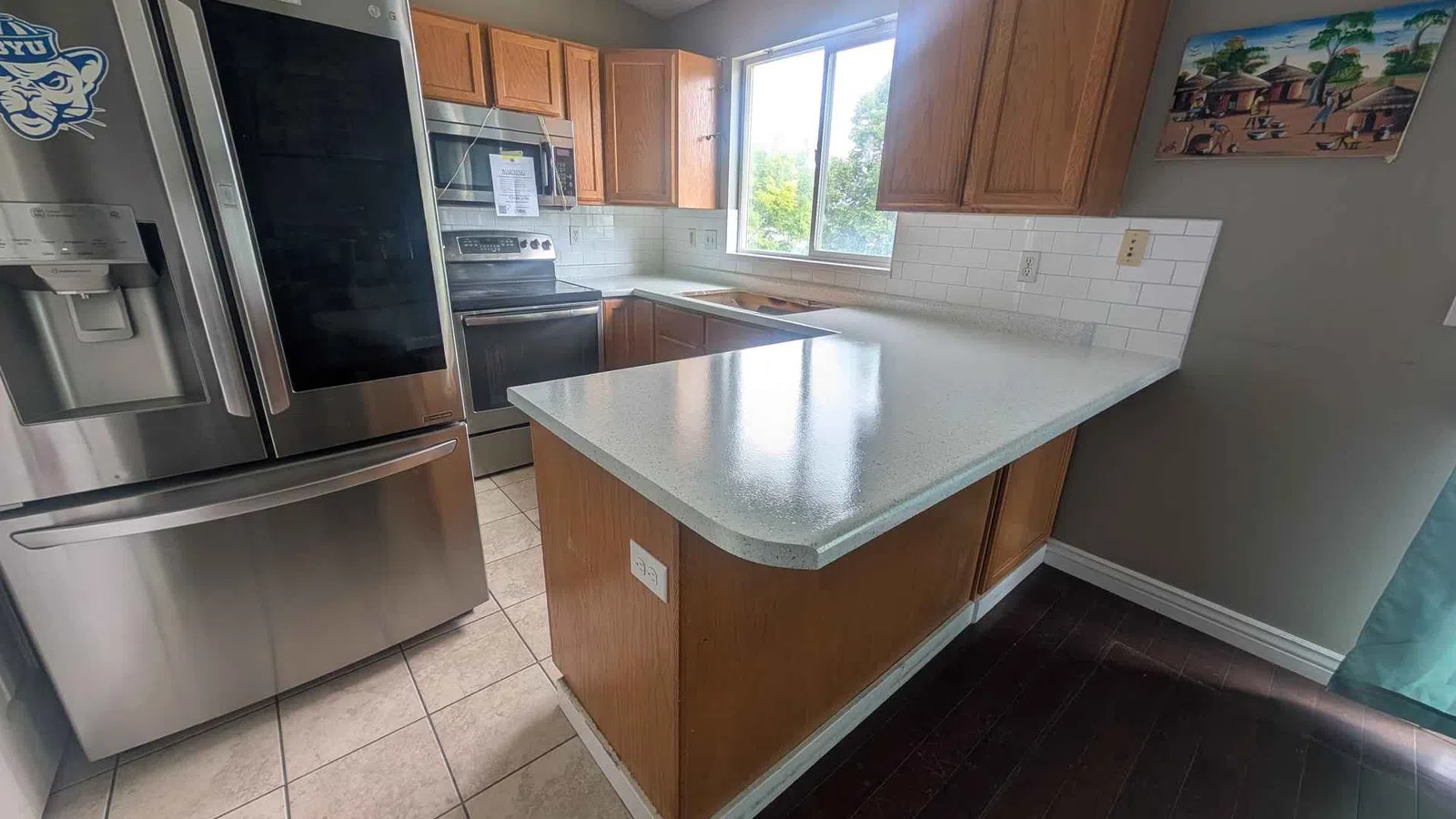 Modern kitchen with stainless steel refrigerator, stove, wooden cabinets, white countertop, and large window.