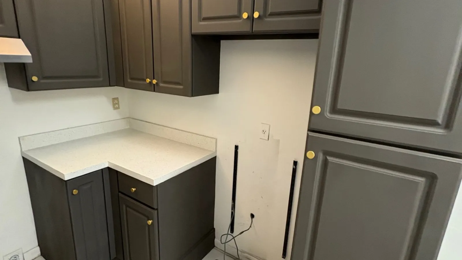 Modern kitchen corner with gray cabinets, white countertop, hexagonal floor tiles, and exposed power outlet with cords.