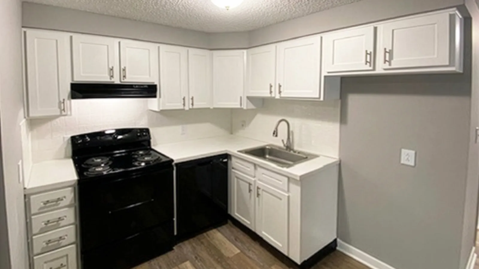 Modern kitchen with white cabinets, black appliances, wood flooring, and a ceiling light fixture.