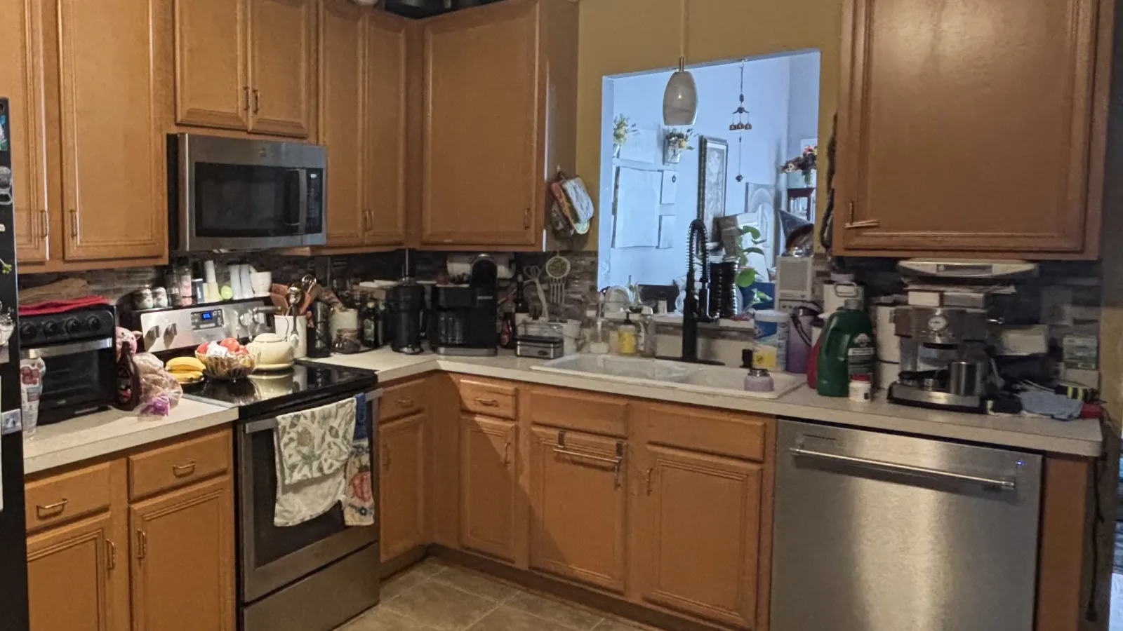 Cozy kitchen with wooden cabinets, stainless steel appliances, and various kitchen gadgets on tiled floor.