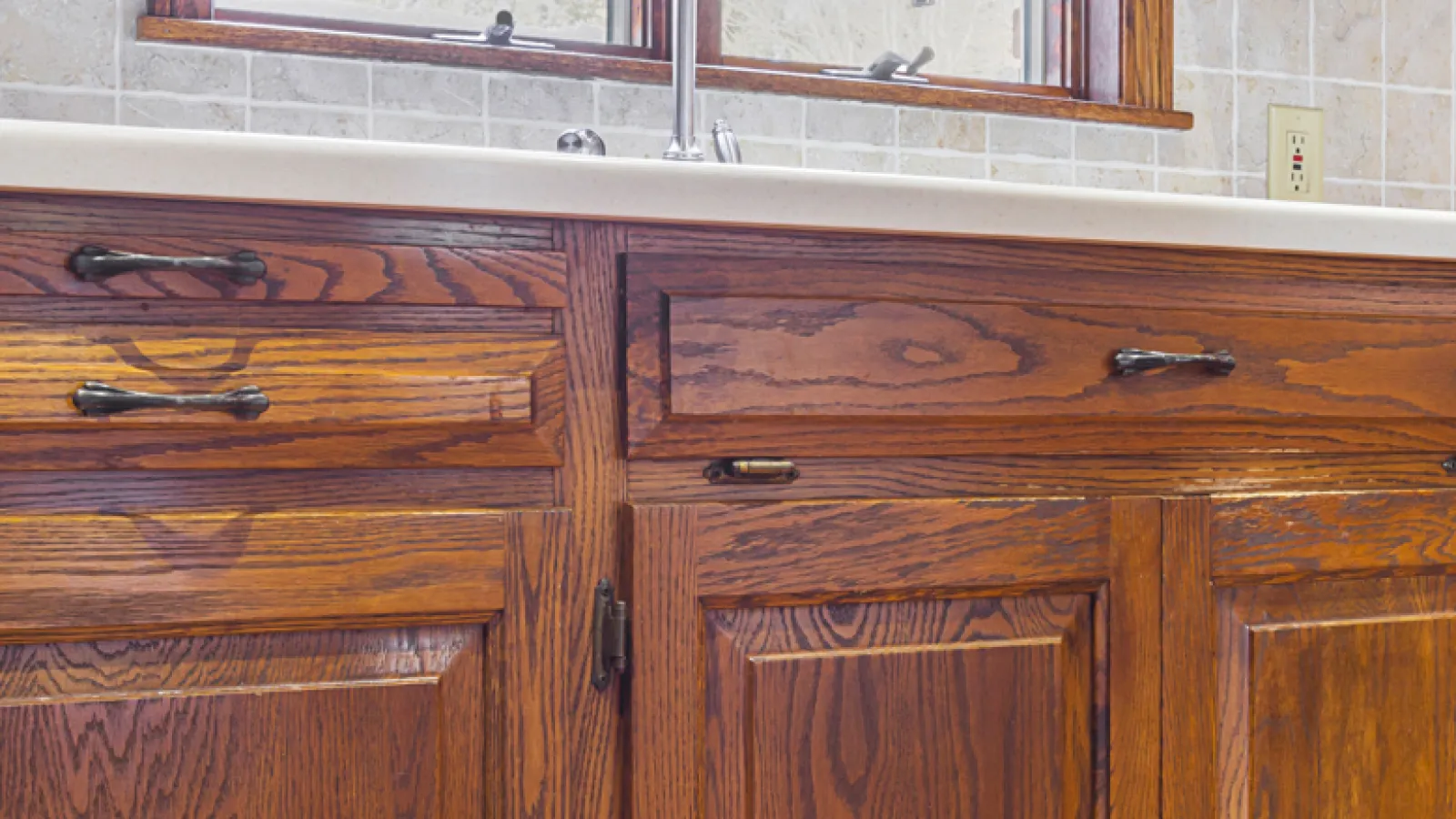 Close-up of wooden kitchen cabinets with metal handles under a white countertop and tiled backsplash.