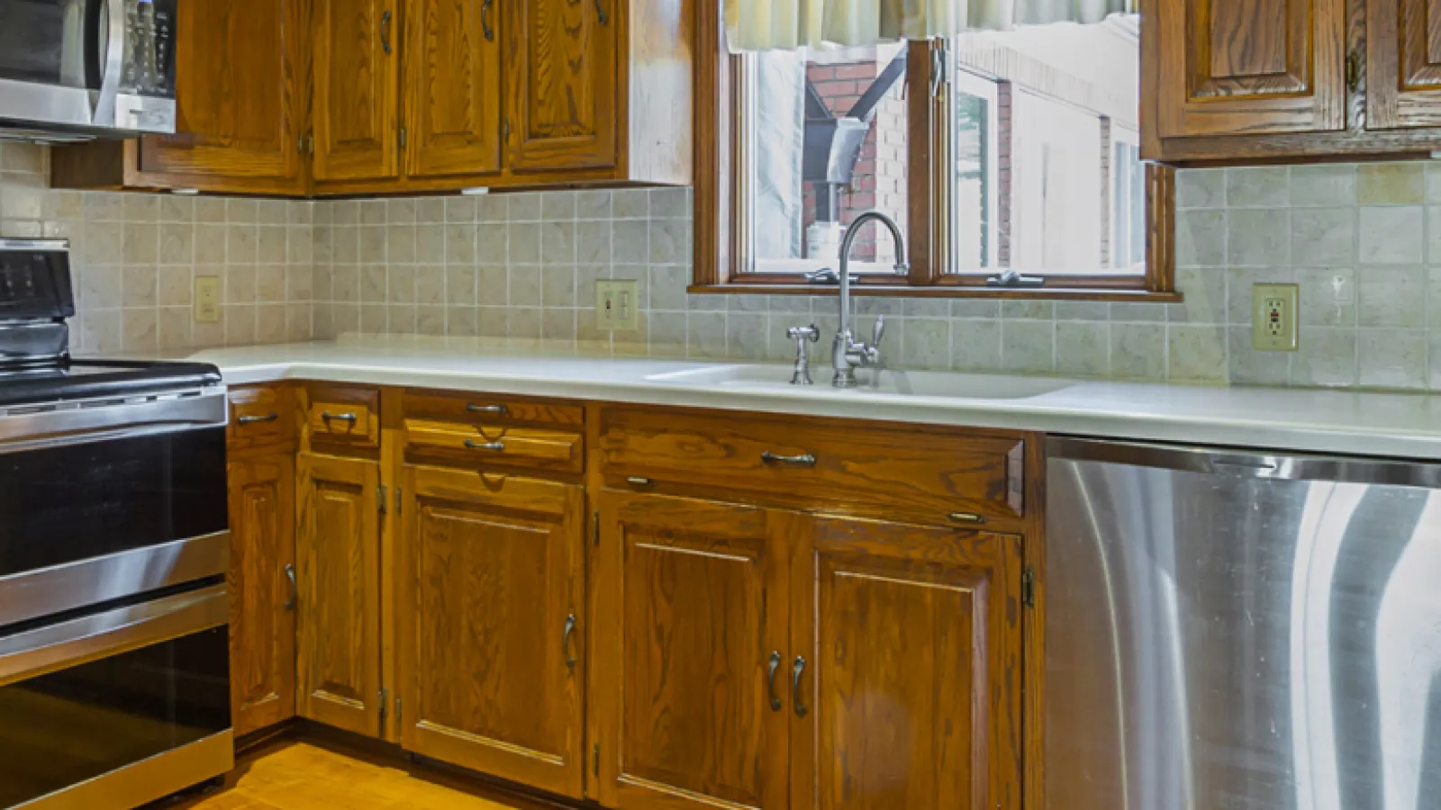 Spacious kitchen with wooden cabinets, stainless steel appliances, tiled backsplash, and large window above sink.