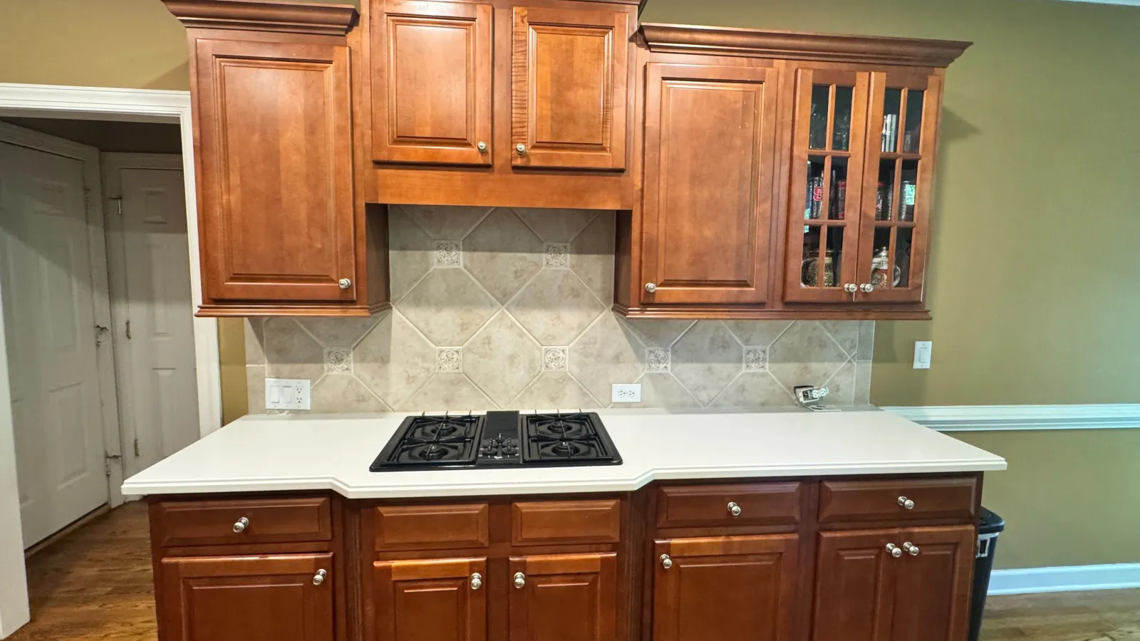 Kitchen with wooden cabinets, white countertop, built-in gas stove, and beige tiled backsplash.
