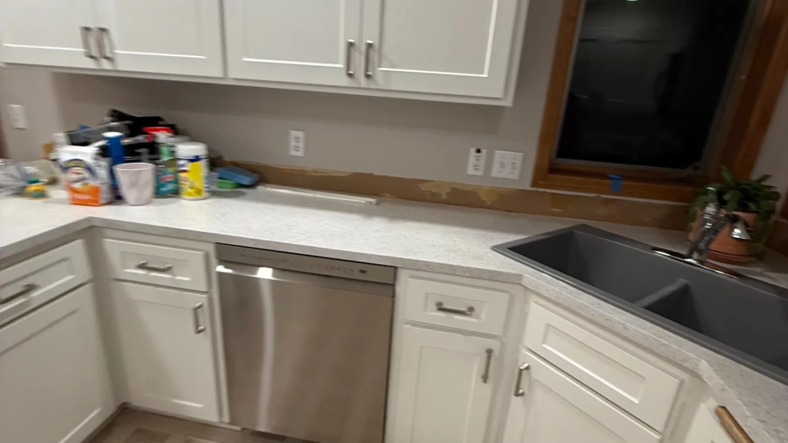 Modern kitchen with white cabinets, stainless steel dishwasher, black sink, and beige patterned tile floor.