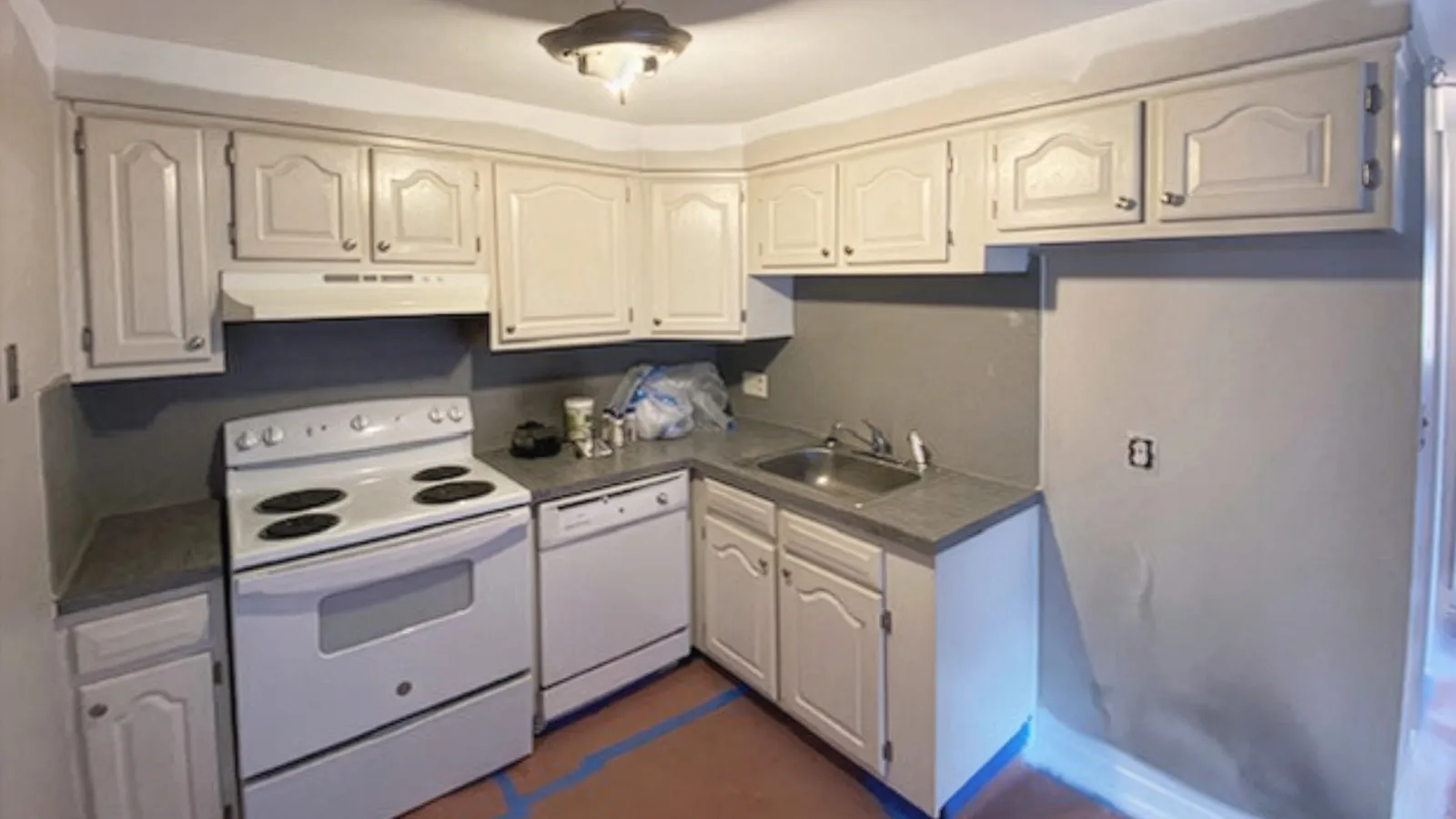 Small kitchen with white cabinets, electric stove, dishwasher, sink, and gray countertops in a compact layout.